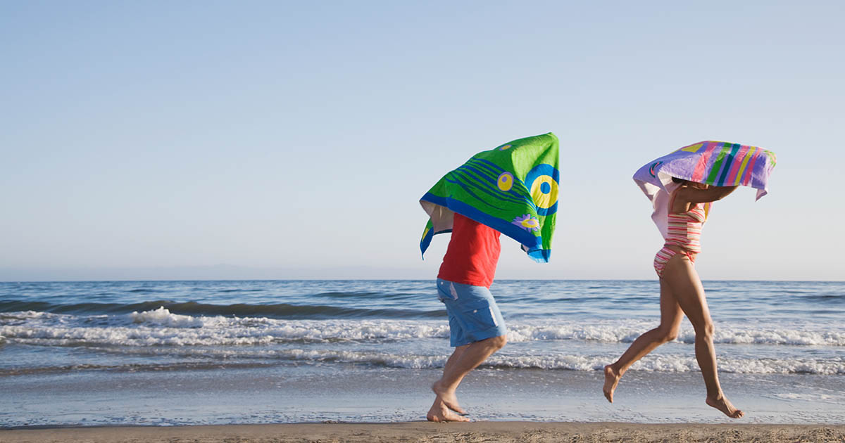 Two kids with microfiber beach towels running by the ocean