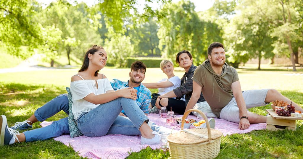 College students enjoyinng an outdoor picnic on a big blanket. Modern picnic blankets and mats have great features that make them a great asset on camping or beach trips.