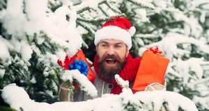 Bearded man, in Santa hat, with gifts hiding in trees.